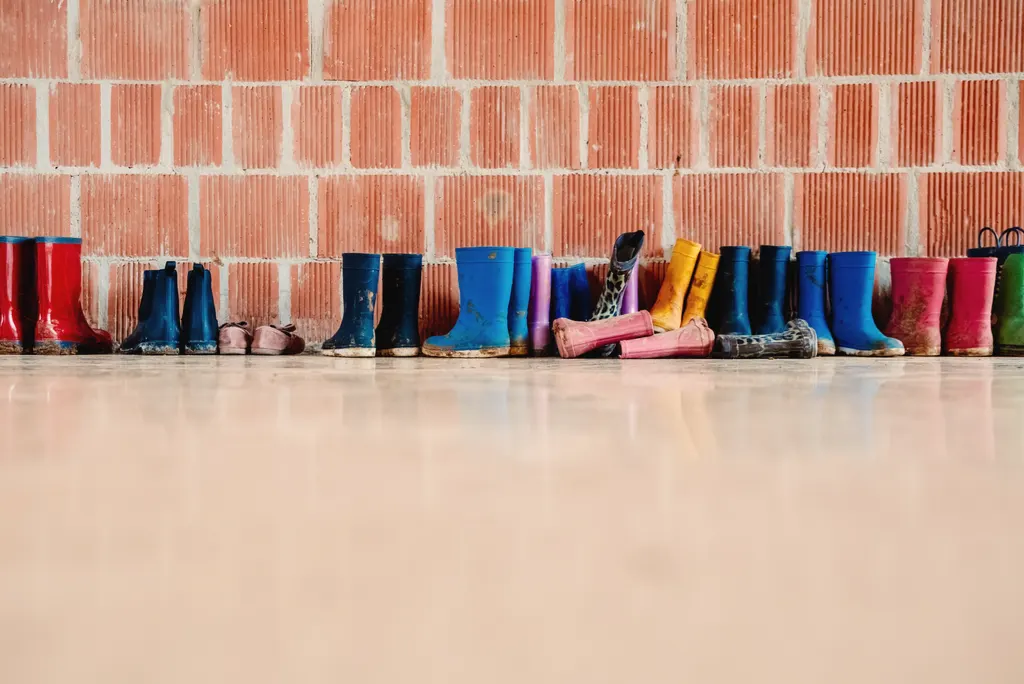 A long row of colourful children's wellies against a brick wall